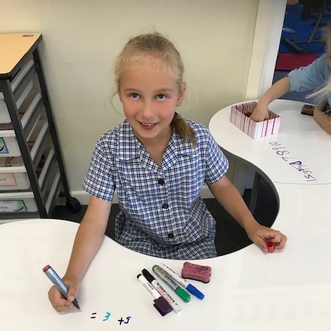 A student sitting at a desk writing with markers.